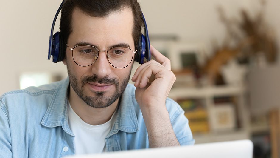 A man holding headphones over his ears while looking at a computer screen