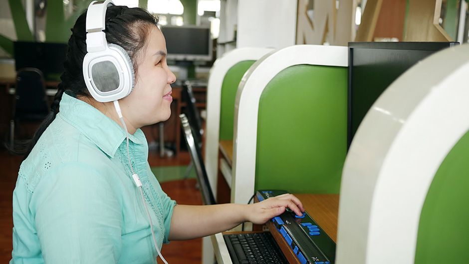 A woman with low visual acuity wearing headphones and usng a modified keyboard