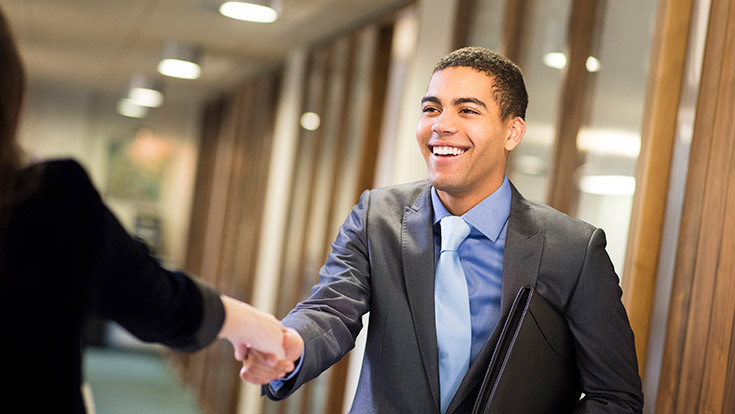 A student wearing a suit extending a hand for a handshake