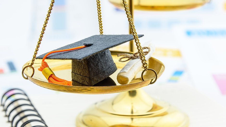 A small graduation cap with an orange tassel and diploma on a legal scale of justice