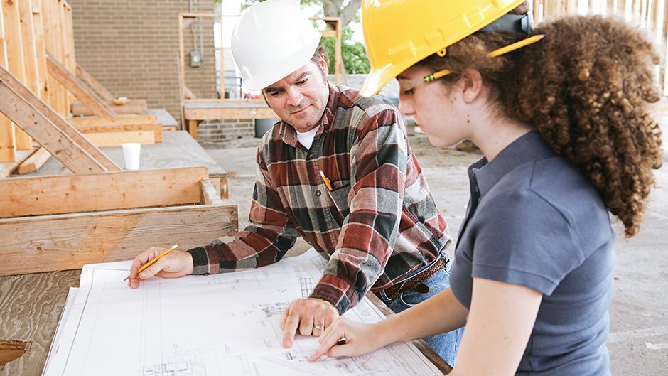 Two students in hardhats looking at building plans