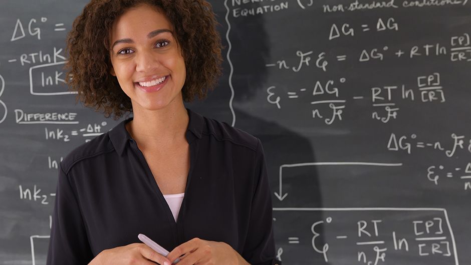 A teacher in front of a chalkboard filled with math equations