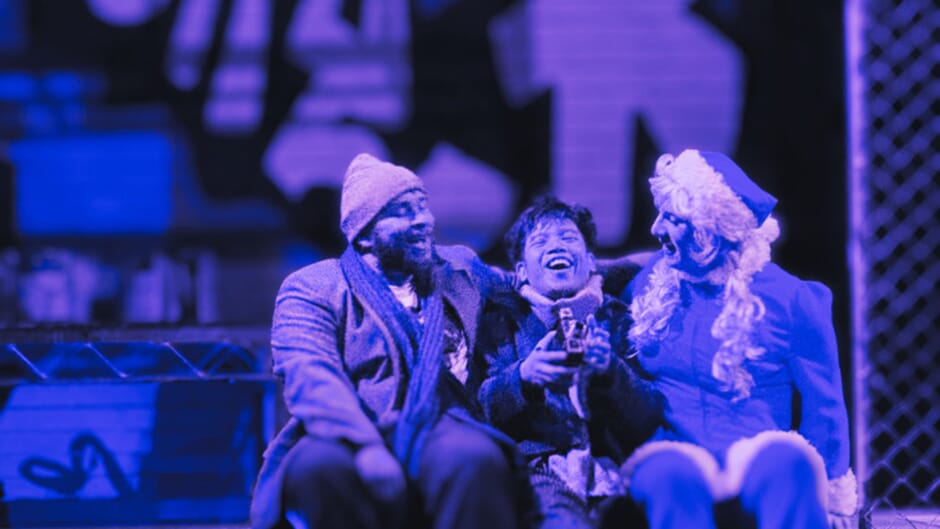 Three actors in winter outfits on a bench on stage