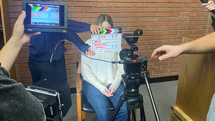 A person holding a clapboard in front of an actor and a camera