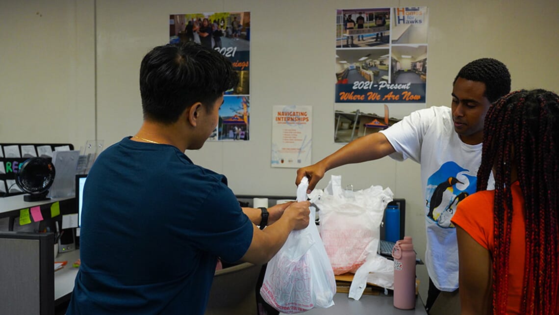 A student passing a bag of groceries to another student inside the Hawk CARES Center