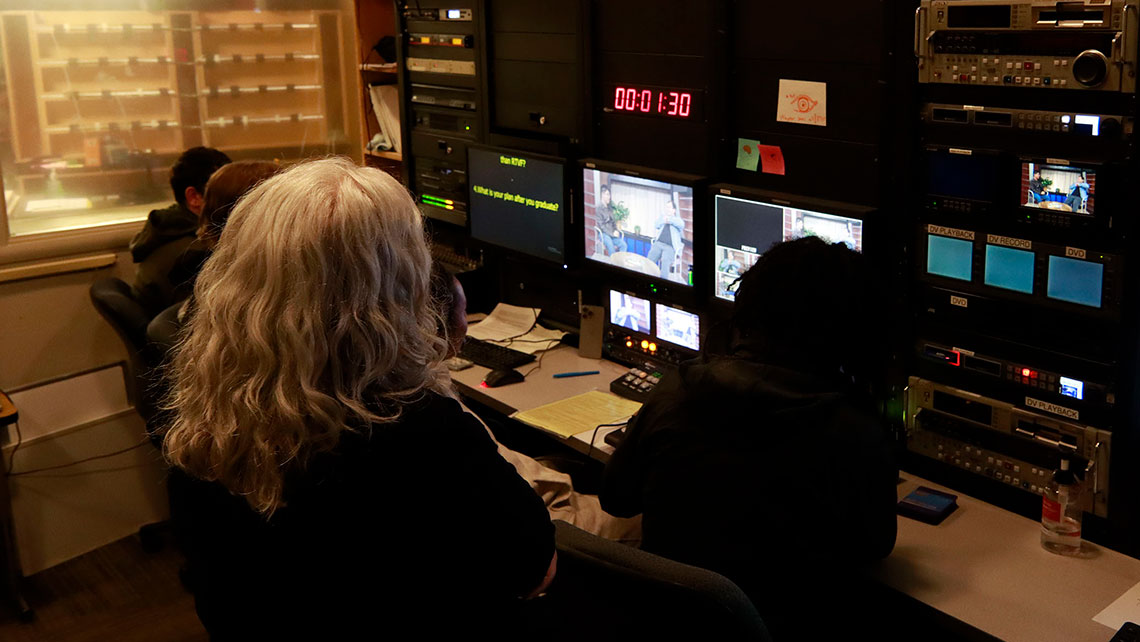 An instructor looking over the shoulders of students working at a production desk
