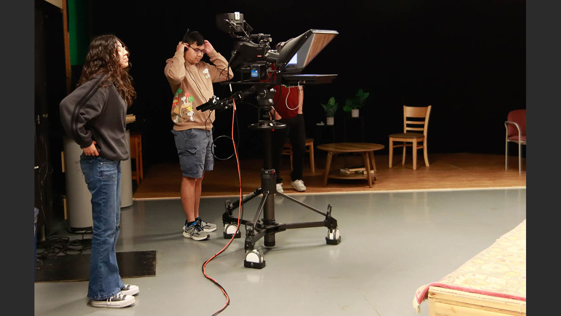 Two students standing off stage, directing and filming