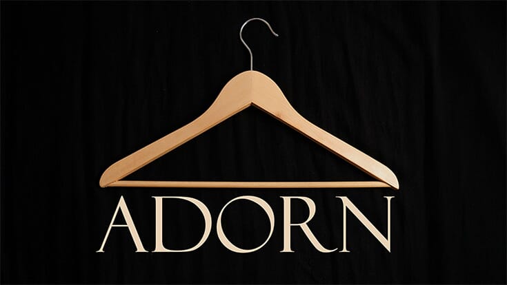 A logo showing a wooden clothes hanger on a black background with the word ADORN