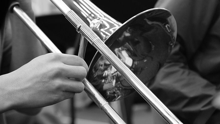 A black and white photo of hands playing a trombone