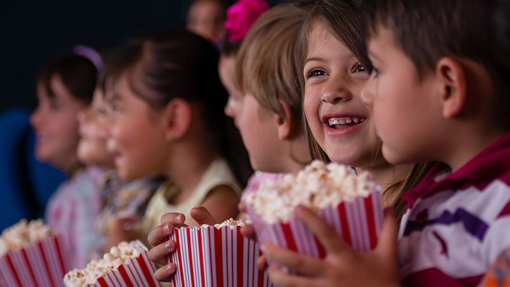 Young children watching a movie and eating popcorn