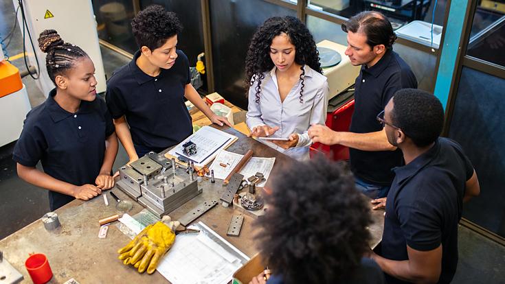 Blue collar workers gathered around a table with parts on it